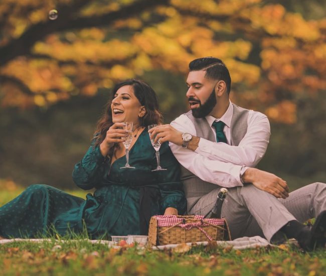 A groom playfully taking a photo of his bride with a professional camera during their fun pre-wedding shoot in a historical garden setting. For Images in the Woods/Autumn
