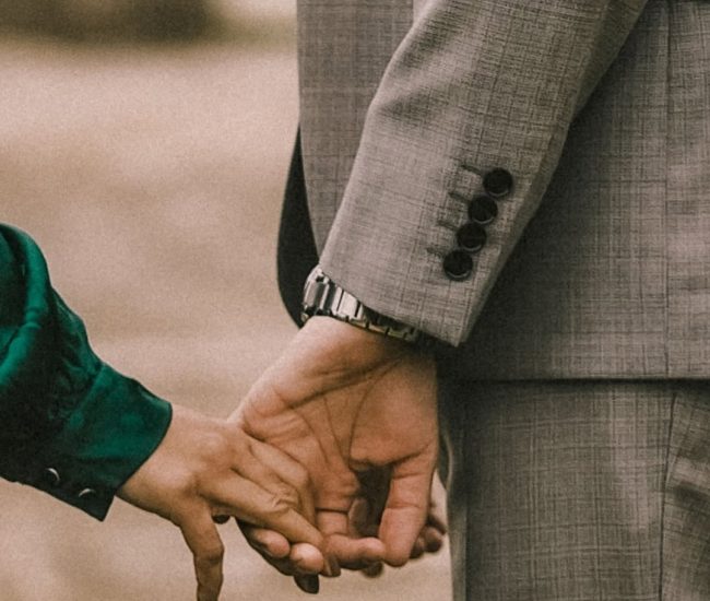A close-up shot of the groom's hand with two birds perched on it, with the bride's hand gently touching his arm.