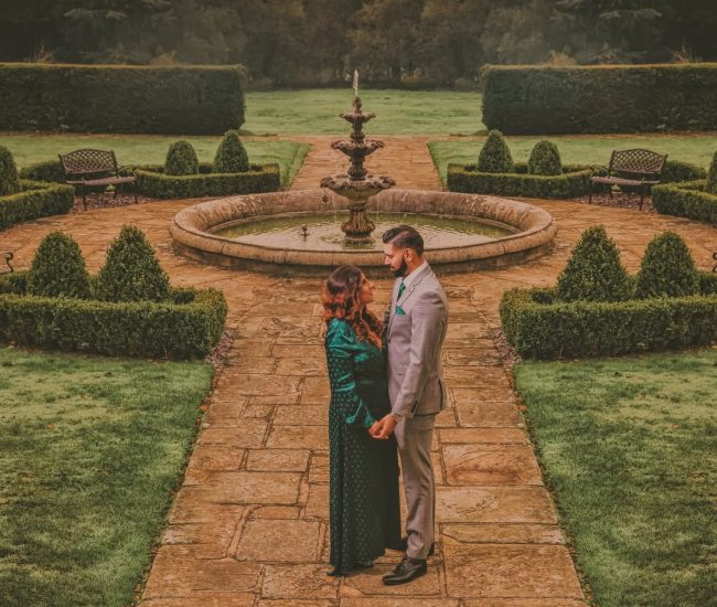 A candid shot of a couple during their pre-wedding shoot, with the bride’s teal dress elegantly fanned out on a blanket surrounded by colorful autumn leaves.