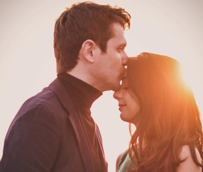 The groom gently kissing his bride's forehead in a loving and intimate moment captured during their elegant couple portrait session.