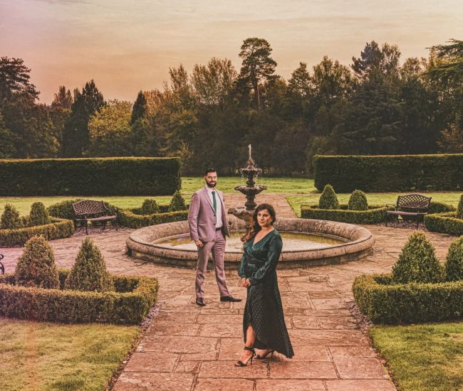 A pre-wedding portrait of the couple standing in front of a grand, highly-detailed black iron gate, showcasing classic architecture.