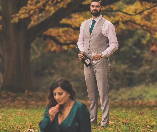 A candid pre-wedding photo of a couple lying on a blanket surrounded by fallen autumn leaves.