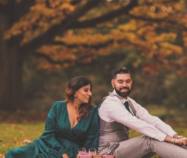 The engaged couple embracing while sitting on the ground amidst fallen autumn leaves in a forest, for a cozy and romantic pre-wedding photoshoot.