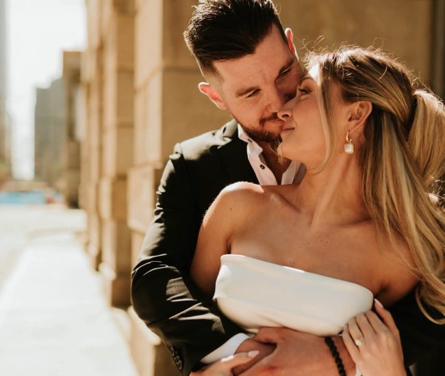 Groom giving a side hug to bride in front of a city tower during Fatography pre wedding photography