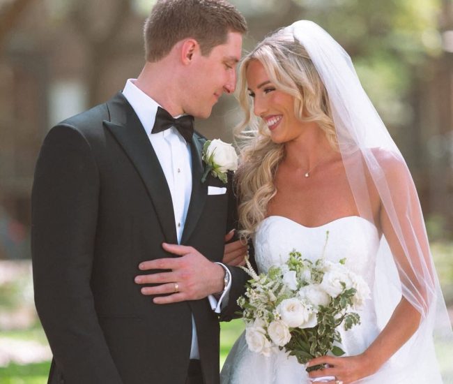 A classic wedding portrait of the bride and groom embracing and smiling, with the groom in a tuxedo and the bride in a white gown.