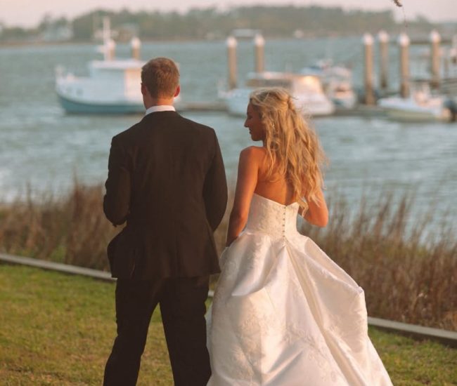 : The bride and groom walking away from the camera toward a beautiful sunny seascape, captured in an elegant wedding portrait.